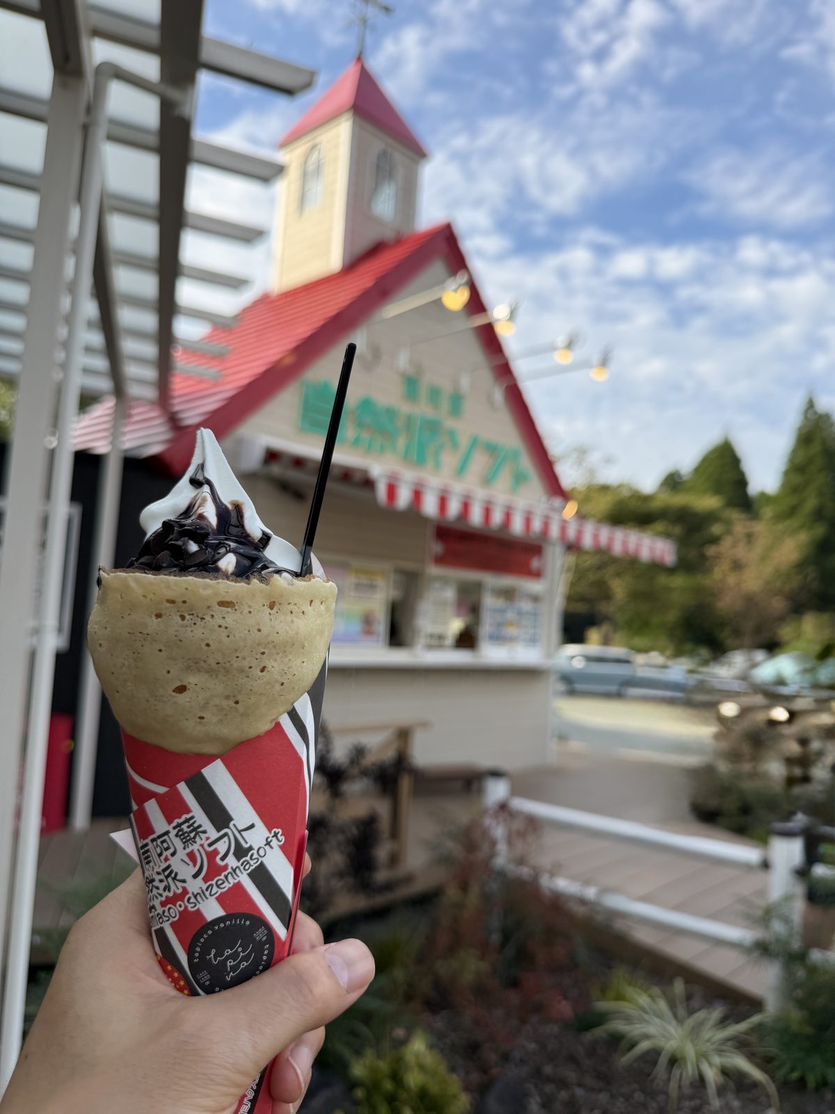 店舗を背景に手に持った追加ソフト入りクレープ「チョコチップ」